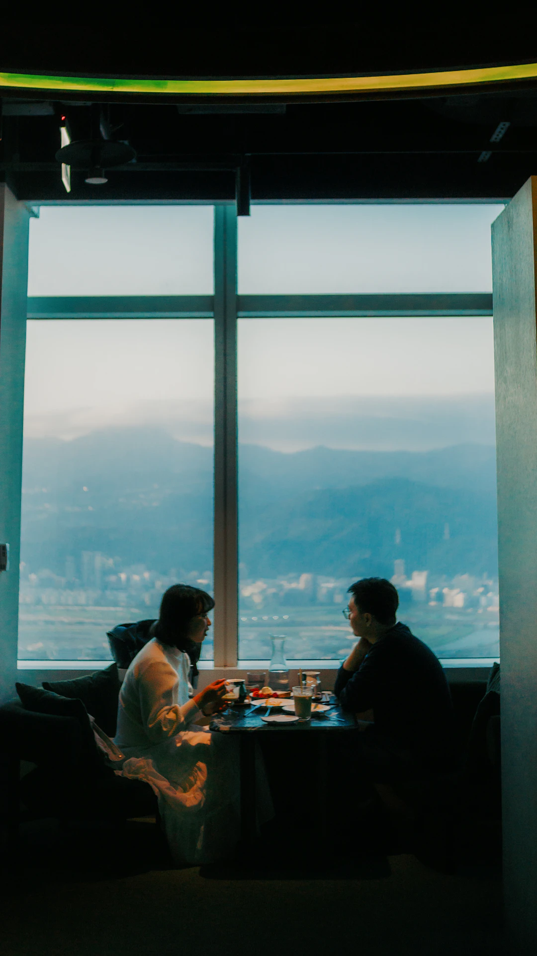 Two people sit at a table by a large window.