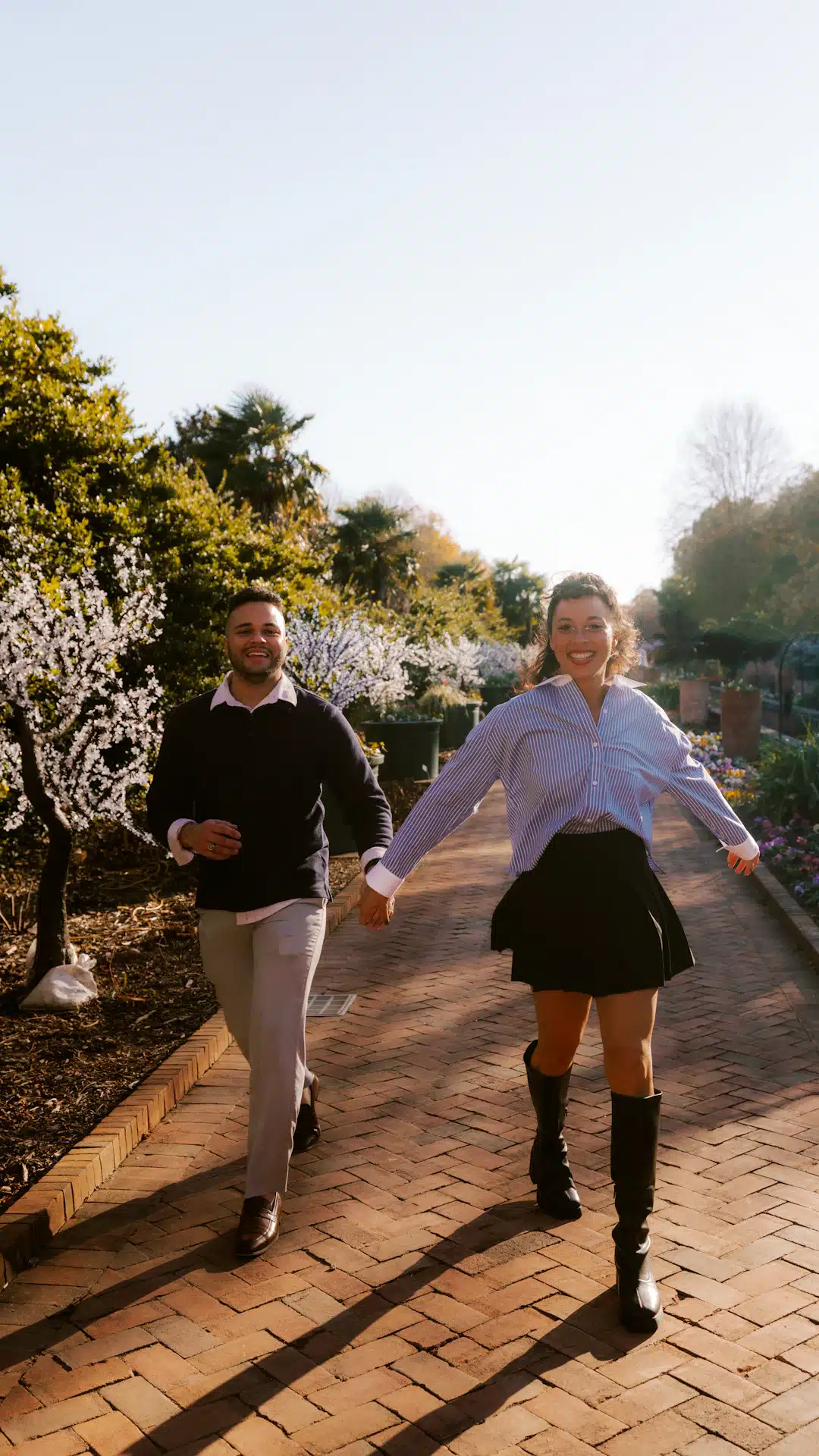 Couple holding hands walking on brick path in park.